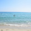 Persone che nuotano in mare calmo con spiaggia sabbiosa in primo piano.
