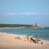 Spiaggia sabbiosa con torre e bagnanti.