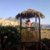 Persona in capanno con tetto di paglia, paesaggio montano sullo sfondo.