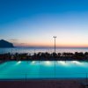 Piscina al tramonto con vista mare e montagna sullo sfondo.