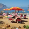 Spiaggia rocciosa con sdraio e ombrelloni colorati.