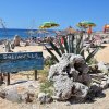 Spiaggia rocciosa con ombrelloni colorati e cactus.