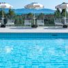 Una piscina con ombrelloni bianchi e sedie a sdraio, vista mare e vegetazione.
