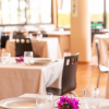 Interno di un ristorante elegante con tavoli apparecchiati, fiori viola e sedie nere.