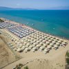 Vista aerea di una spiaggia affollata con file di ombrelloni e lettini, vicino al mare turchese.