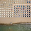 Spiaggia sabbiosa vista dall'alto, con file ordinate di ombrelloni e lettini.