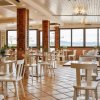 Ristorante luminoso, tavoli e sedie bianchi, finestre ampie con vista esterna.