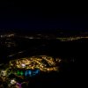 Vista notturna di un complesso luminoso in un paesaggio collinare con cielo stellato.
