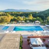 Piscina all'aperto con ombrelloni bianchi, vista su colline verdi e un'isola in lontananza.