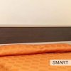 Letto singolo con copriletto arancione e testiera scura.