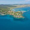 Vista aerea di una penisola con case, scogli e barche, mare blu.