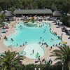Ampia vista di una piscina affollata con giochi d'acqua. Palme e ombrelloni circondano la zona.