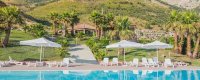 Piscina con lettini e ombrelloni, vista su montagne e palme.