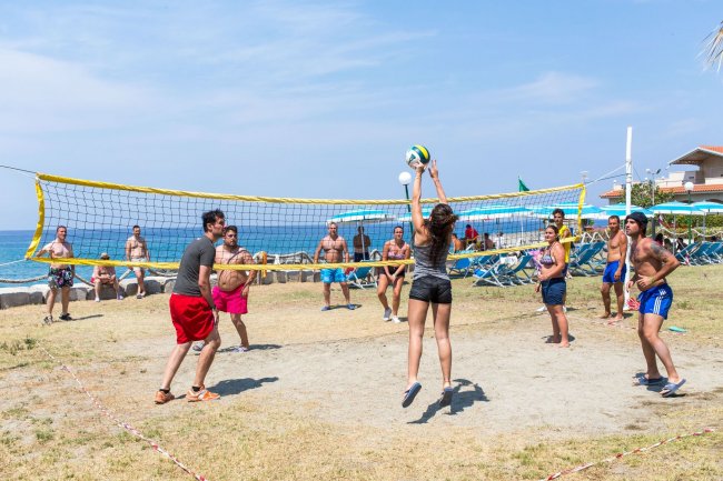 Persone giocano a beach volley vicino al mare.