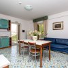 Cucina-soggiorno con mobili blu, tavolo rettangolare, divano blu. Porta aperta su balcone.