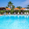 Piscina all'aperto con ombrelloni arancioni e bianchi, circondata da palme e sedie a sdraio.