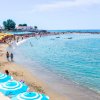 Spiaggia affollata con mare calmo, ombrelloni azzurri e gialli lungo la costa.
