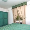 Armadio verde, sedia e letto in una stanza con tende beige e pavimento decorato.