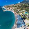 Spiaggia affollata con ombrelloni blu, mare e colline circostanti.