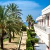 Viale alberato con palme, vista sul mare tra edifici con balconi.