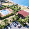 Vista aerea di una piscina con ombrelloni arancioni vicino al mare e palme.