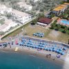 Spiaggia con ombrelloni blu, vicino a edifici con una piscina e giardino.