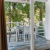 Balcone con tavolo apparecchiato, sedie bianche e vista sul giardino alberato.