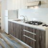 Cucina moderna con pensili in legno scuro, piano cottura e lavello. Bagno sullo sfondo.