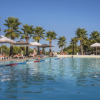Piscina all'aperto circondata da palme e ombrelloni, persone che nuotano e si rilassano.