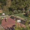 Campo da basket all'aperto accanto a un'area giochi per bambini, circondati da vegetazione.