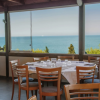 Ristorante con tavoli apparecchiati davanti a grandi finestre con vista sul mare e vegetazione.