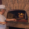 Uomo con cappello bianco inforna in un forno a legna di mattoni.