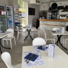 Interno di bar moderno con tavoli apparecchiati e frigoriferi visibili.