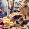 Persone scelgono prodotti da un tavolo con pane, dolci e marmellate in un mercato all'aperto.
