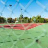 Campo da tennis visto attraverso una rete metallica.