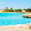 Costa rocciosa e mare cristallino in un giorno soleggiato.