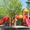 Parco giochi colorato con scivolo e alberi.