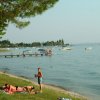Riva di un lago con persone che prendono il sole e barche in acqua.