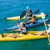 Persone che remano in kayak gialli e blu su acqua limpida.