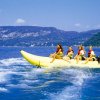 Gruppo su un banana boat giallo in un lago con montagne sullo sfondo.