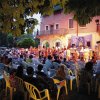 Spettatori seduti assistono a uno spettacolo serale all'aperto.