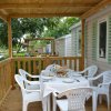 Tavolo apparecchiato su veranda di legno, sedie bianche intorno.