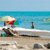 Spiaggia con ombrellone colorato, sdraio e bagnanti nel mare.
