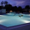Piscina illuminata di notte con bagnanti.