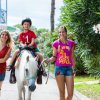Due donne e due bambini, uno a cavallo, camminano su un sentiero alberato.