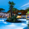 Piscina illuminata di notte con palme e scivolo colorato, circondata da alberi.