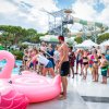 Una piscina con un grande gonfiabile rosa, molte persone in fila accanto.