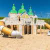 Struttura da gioco simile a un castello con scivoli su una spiaggia sabbiosa.