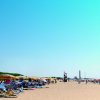 Spiaggia con ombrelloni colorati, lettini e un faro in lontananza.