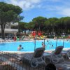 Piscina all'aperto con lettini bianchi, circondata da pini e scivoli gialli e rossi in lontananza.